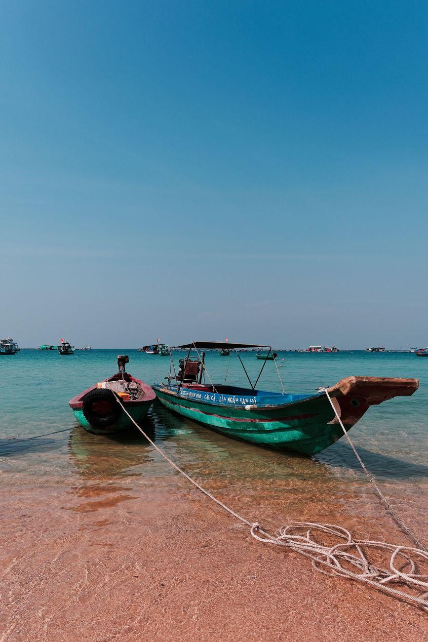 Two fishing boats tied up on a sandy beach with rope in the foreground