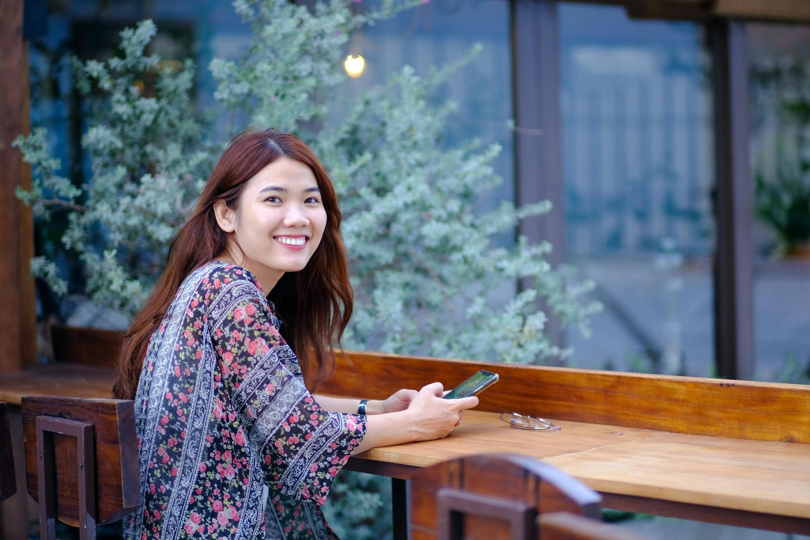 A woman smiling over her shoulder at a wooden cafe table with a phone in hand
