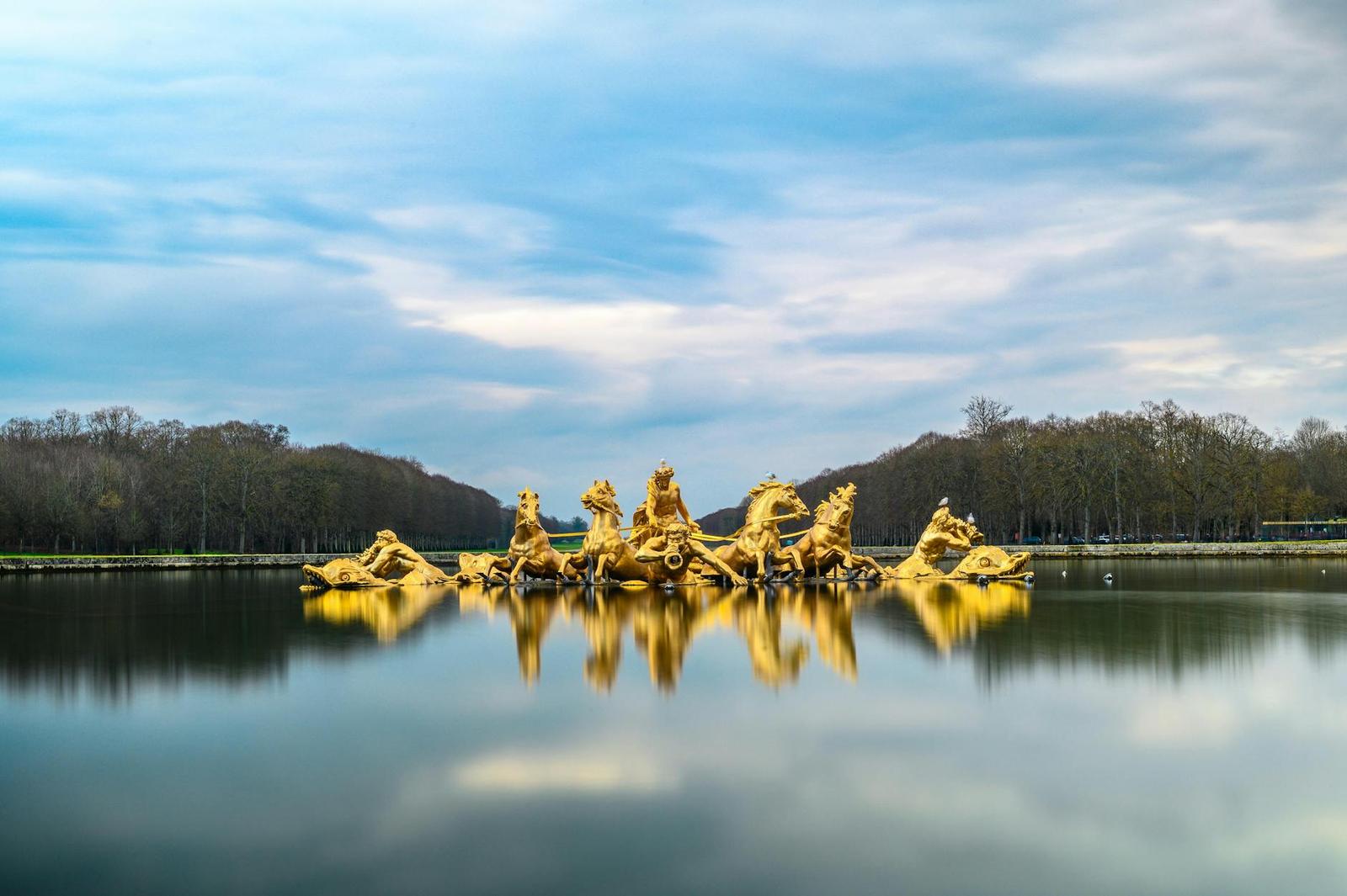 Gilded fountain sculpture of horses reflected in a still palace pool