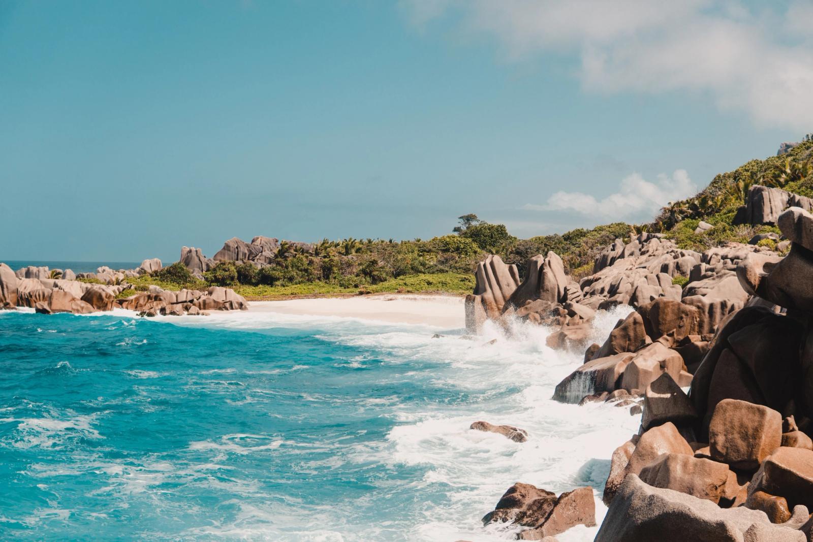 Waves breaking over granite boulders along a turquoise tropical shoreline