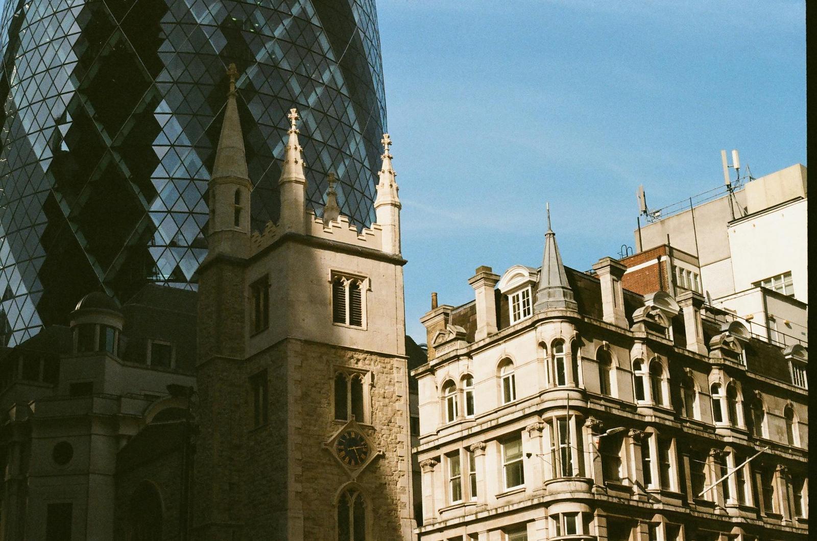 An ornate stone church tower beside a glass egg-shaped skyscraper and period buildings