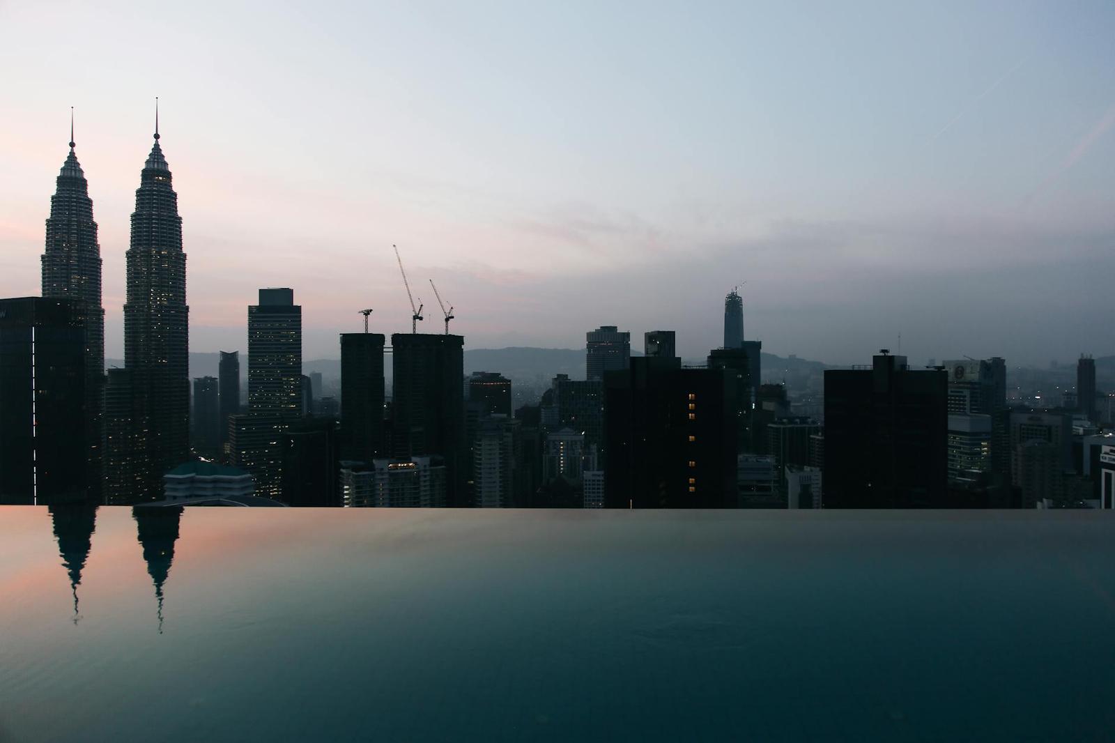 An infinity pool overlooking a city skyline with twin towers at dusk
