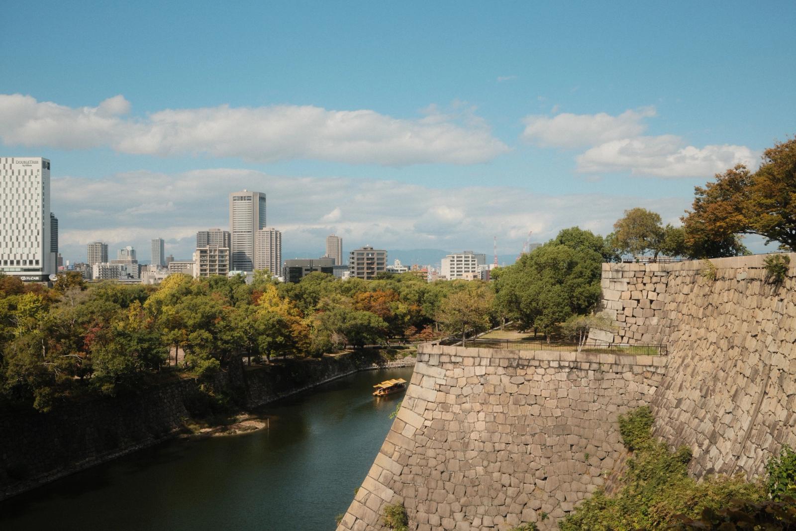 Scenic view of Osaka's skyline with a historic moat and wall, showcasing a blend of nature and urban architecture