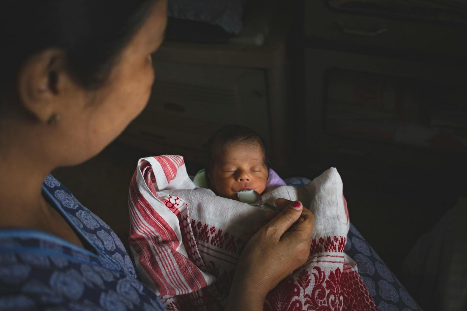 A woman cradles a sleeping newborn wrapped in a patterned cloth