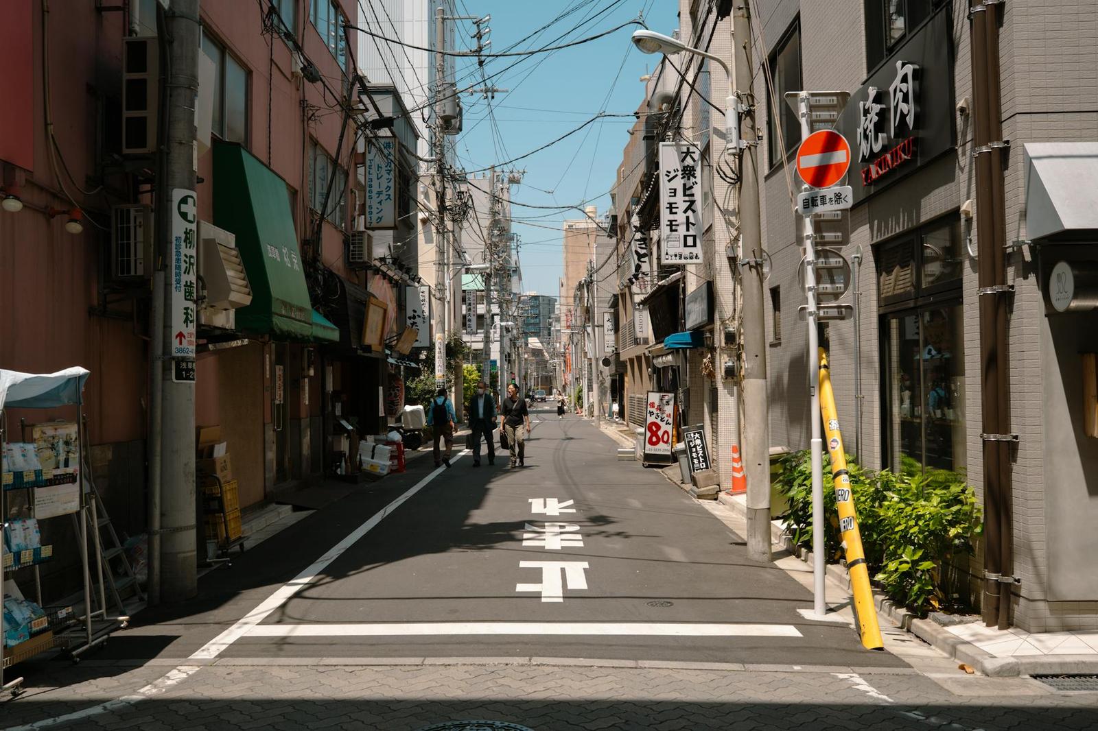 A quiet narrow street lined with shopfronts under overhead wires