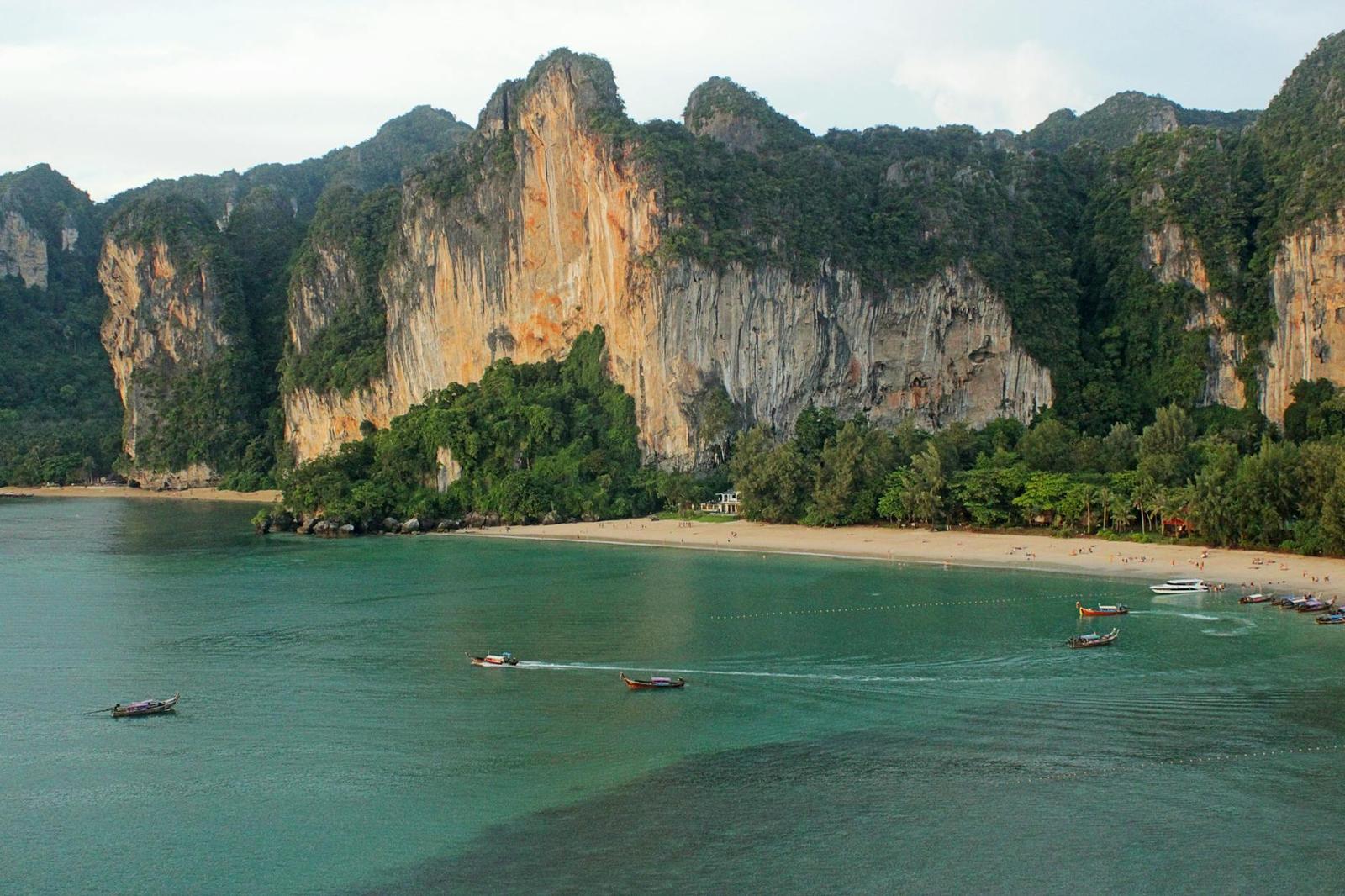 Longtail boats crossing a bay beneath sheer limestone cliffs