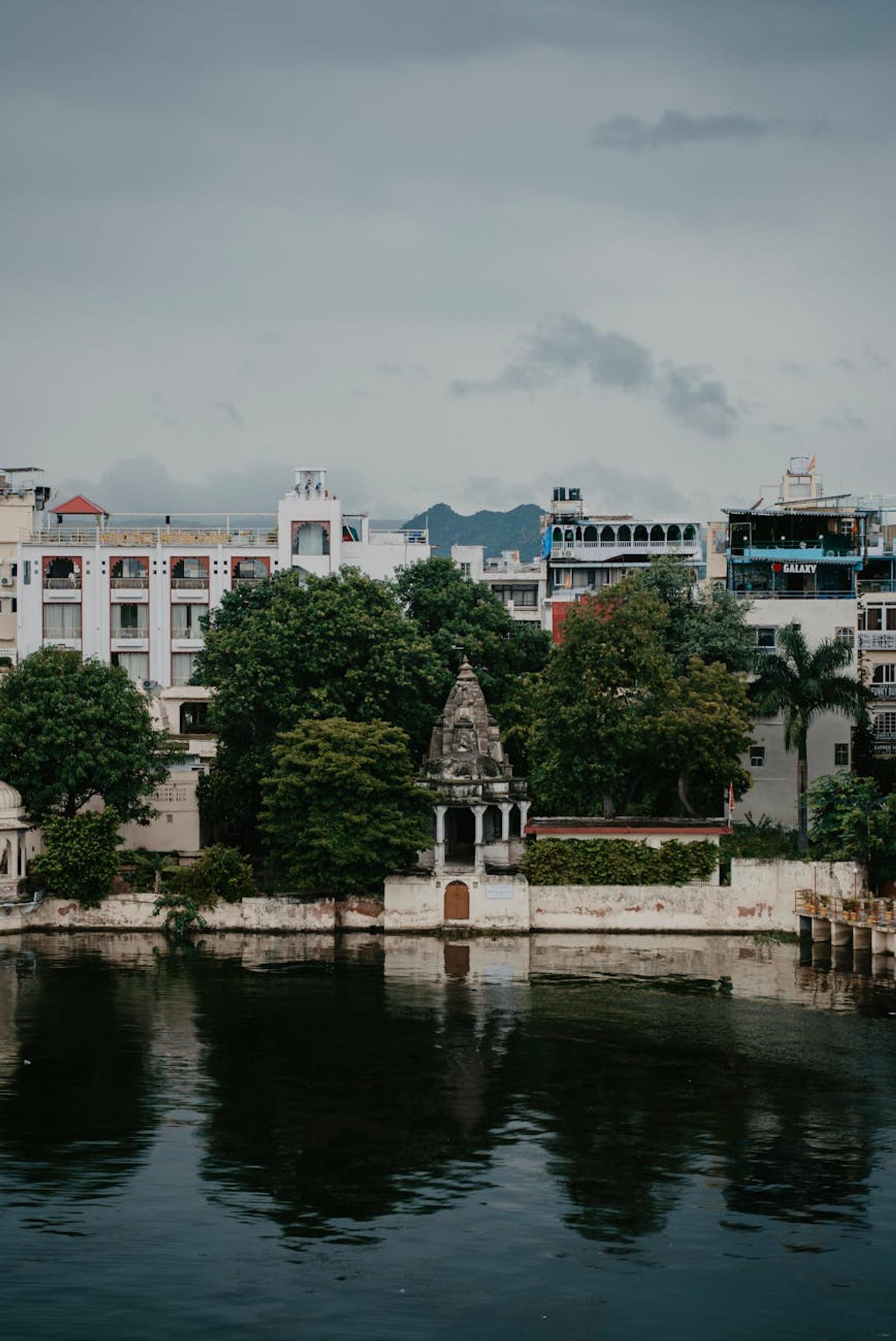 Domed white shrine and lakeside buildings framed by trees and reflection