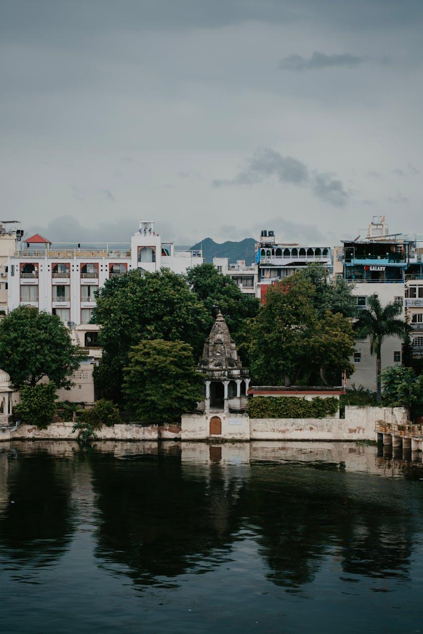 Domed white shrine and lakeside buildings framed by trees and reflection