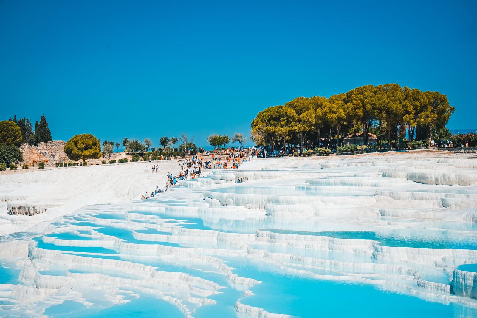 Visitors walking across white travertine terraces under a bright sky