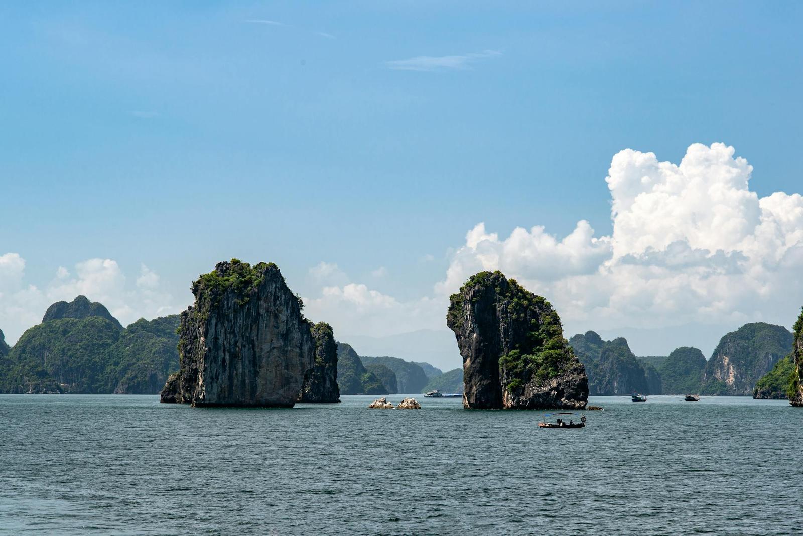 Two limestone islets rising from calm bay water with small boats nearby