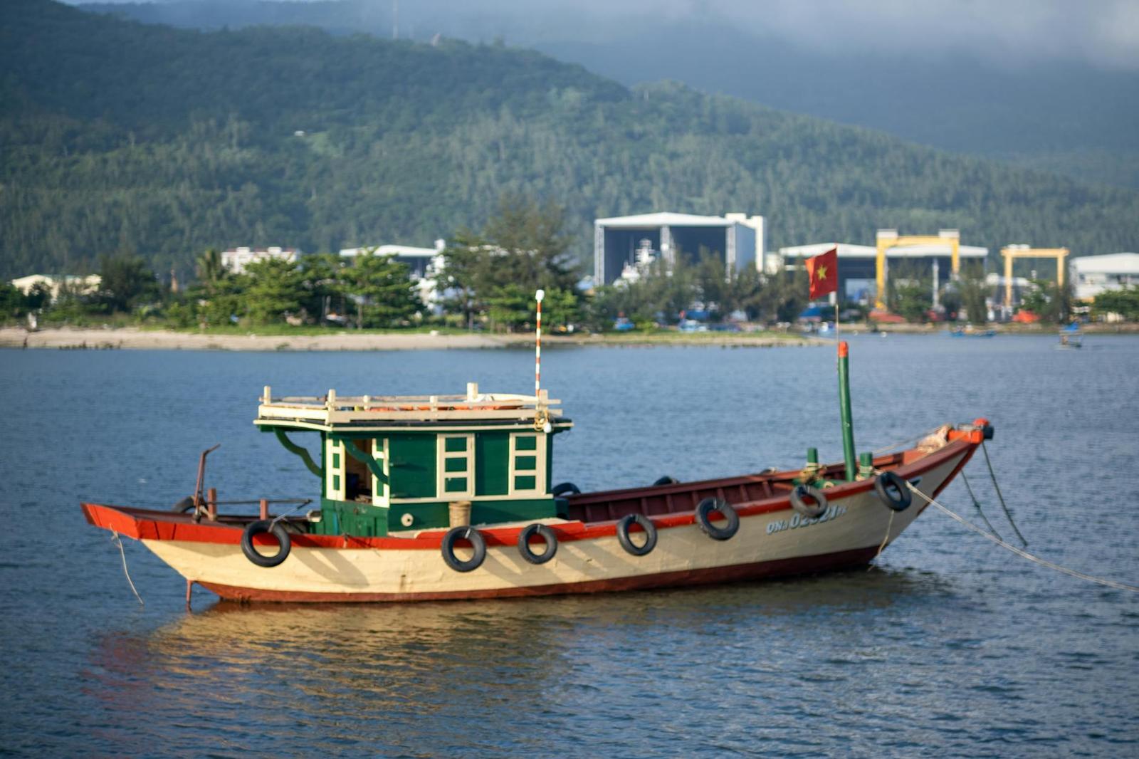 A green wooden fishing boat anchored offshore with a hazy coastline behind