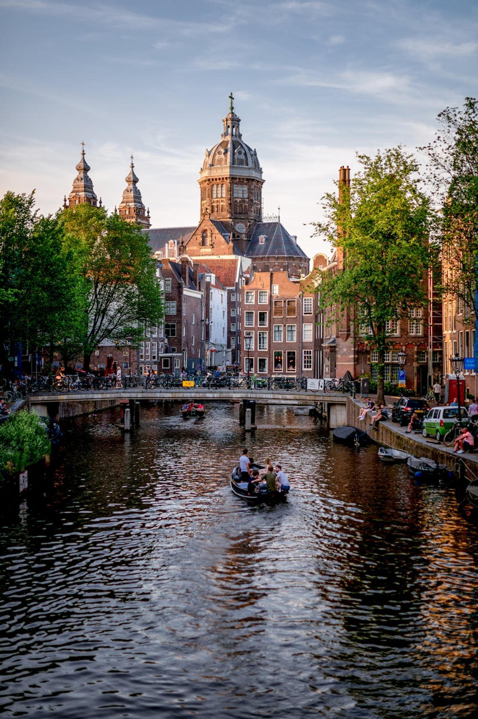 Scenic view of Amsterdam canal with boats and historic buildings, featuring the prominent church in summer