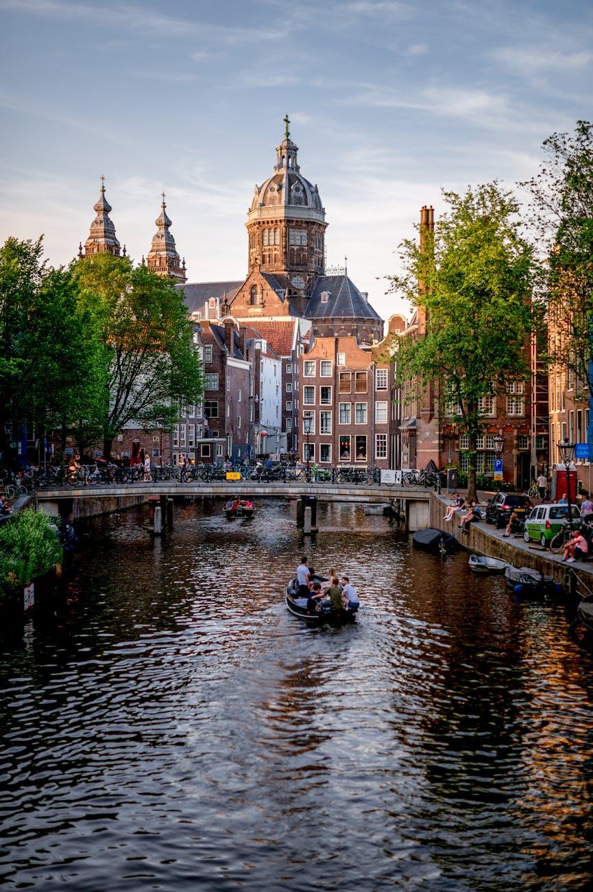 Scenic view of Amsterdam canal with boats and historic buildings, featuring the prominent church in summer