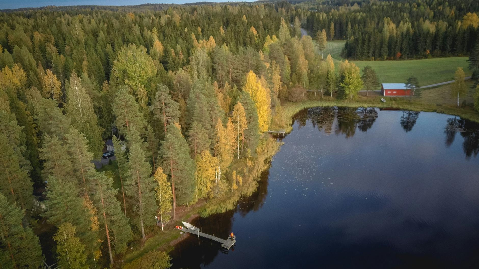 Aerial view of an autumn forest lake with a red cottage