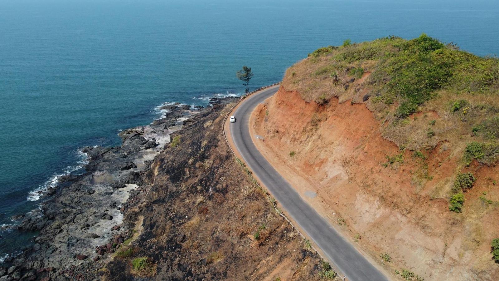 Aerial view of a coastal road curving along red cliffs above the sea