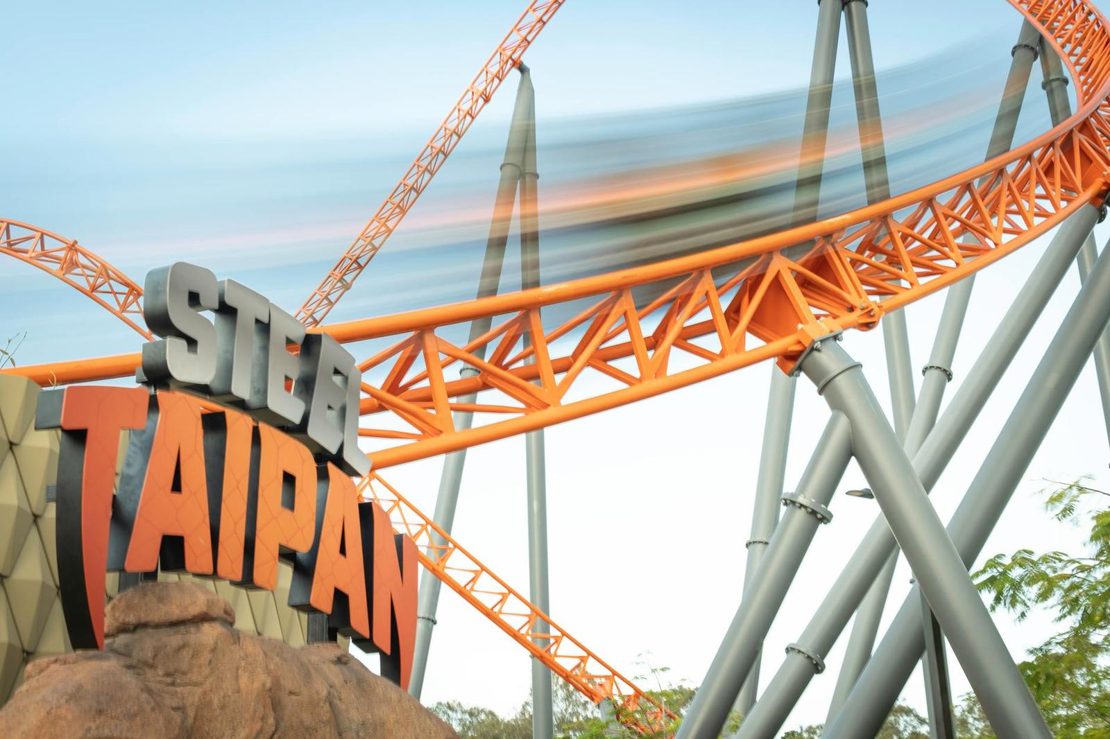 Orange steel rollercoaster track speeding past its signage