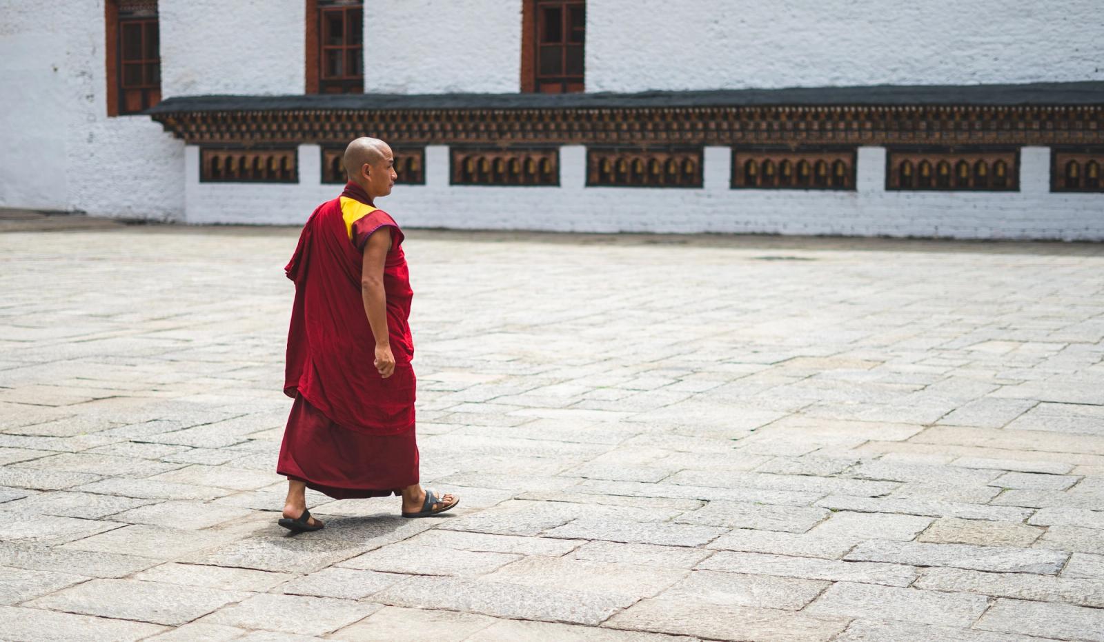 A Buddhist monk in traditional attire walks through a courtyard in Bhutan, showcasing spiritual tranquility