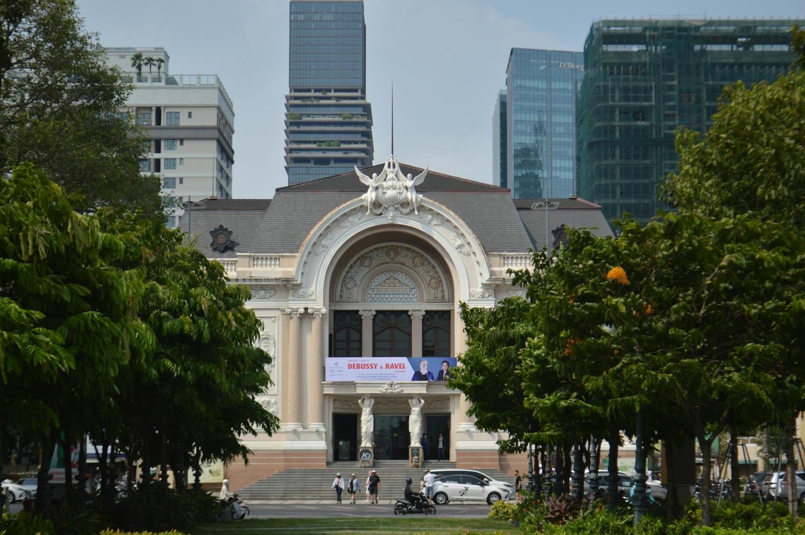 Ornate colonial theatre facade framed by trees with skyscrapers rising behind