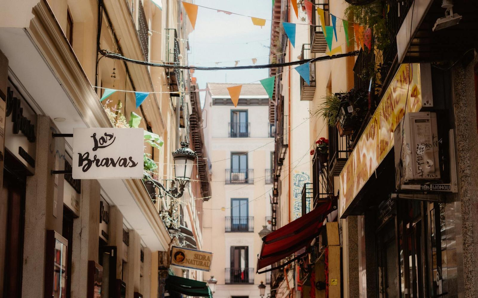 A narrow shopping street strung with colourful festival bunting between tall buildings