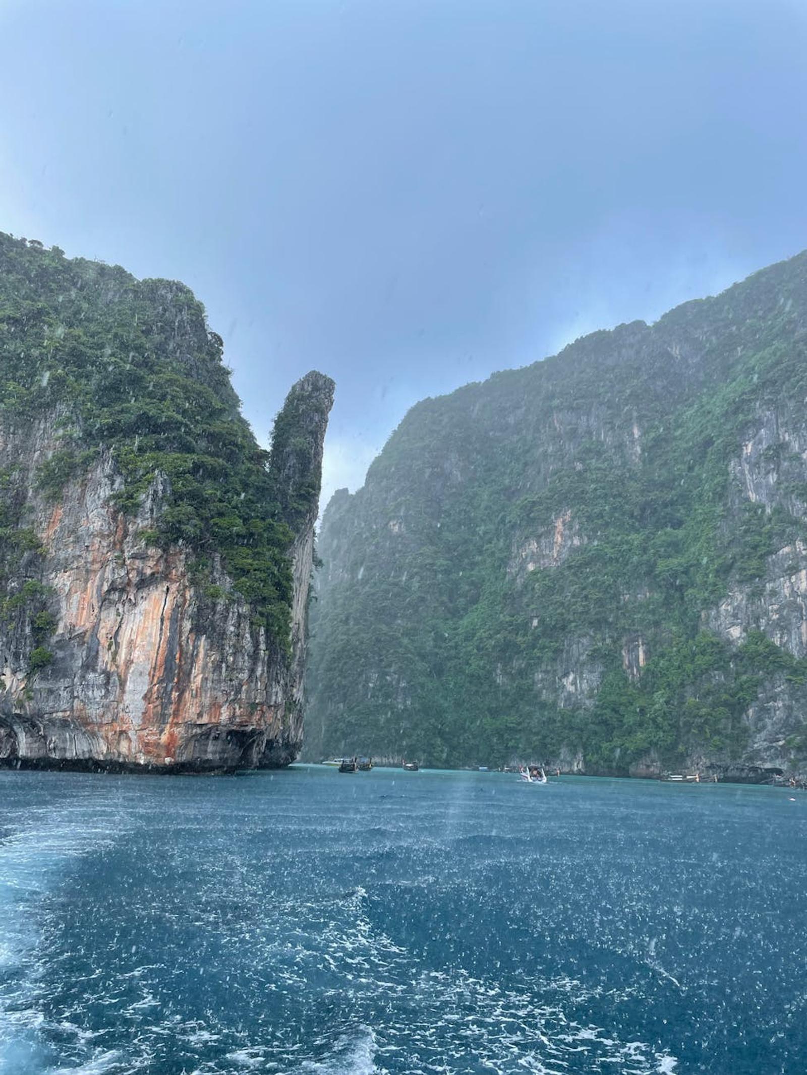 A dramatic cliff landscape with lush greenery and a turbulent sea under rainy skies
