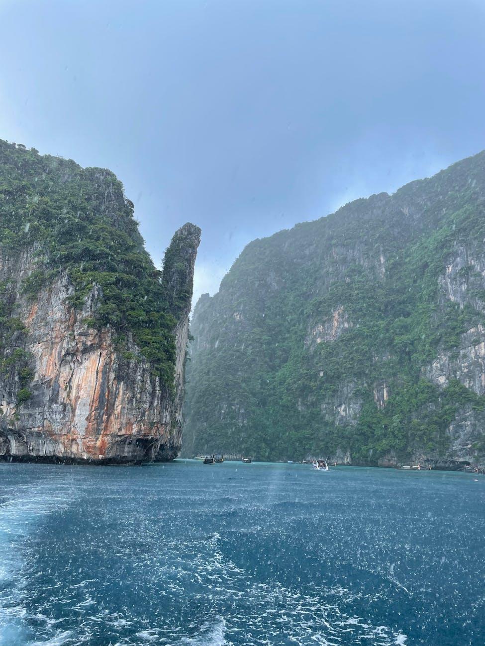 A dramatic cliff landscape with lush greenery and a turbulent sea under rainy skies