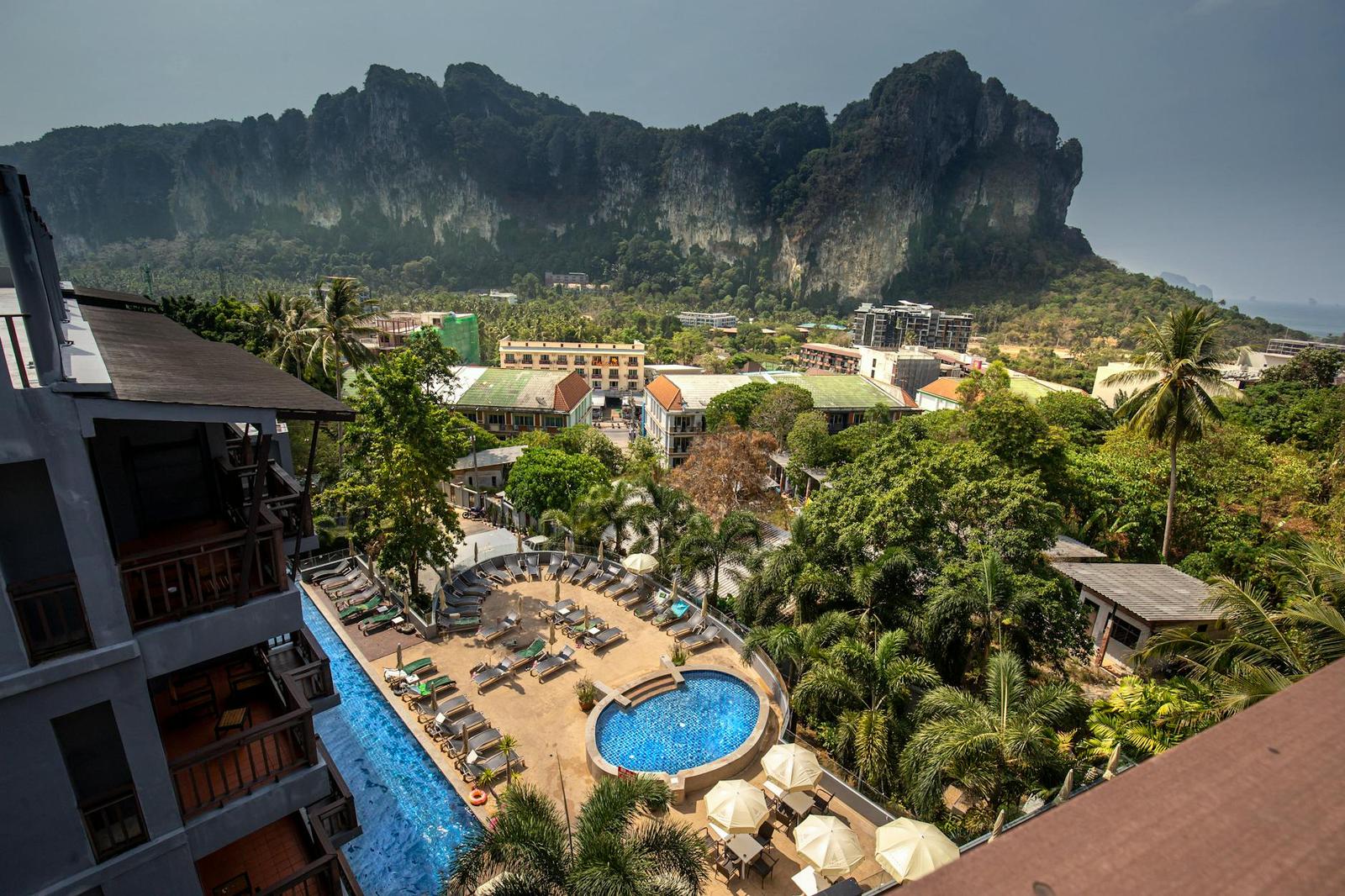 Aerial view of a resort swimming pool surrounded by palm trees below jagged limestone cliffs