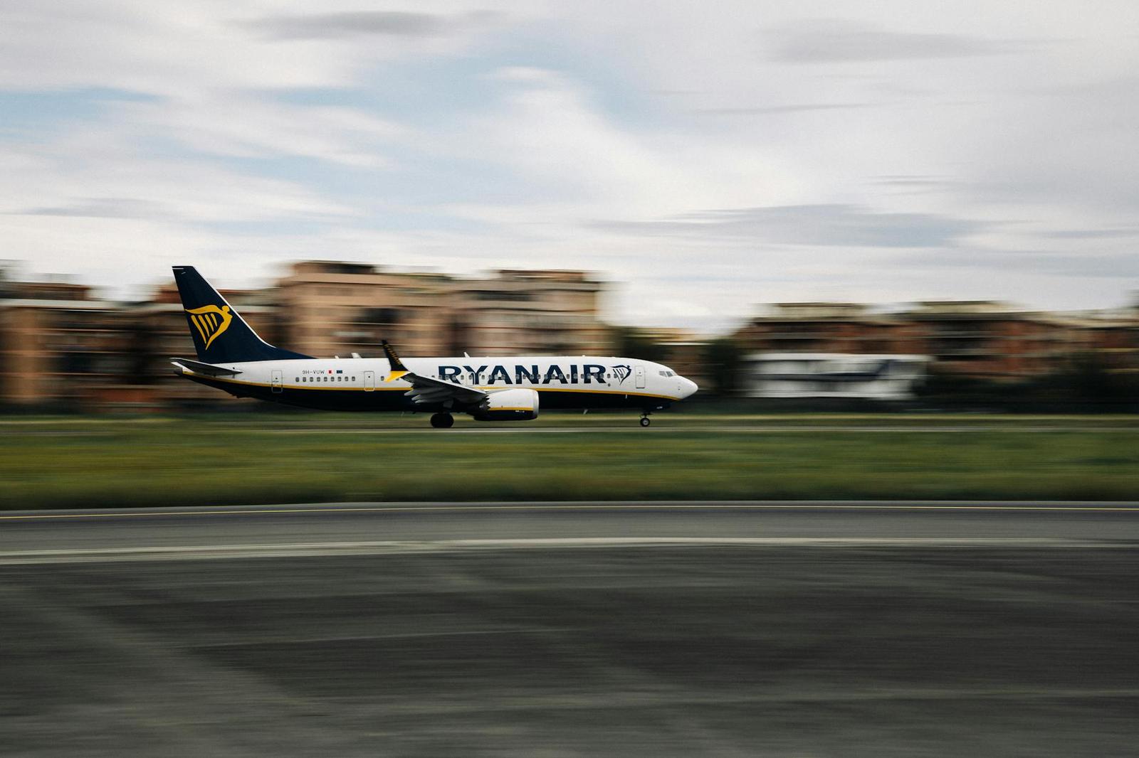 A low-flying passenger jet blurred against buildings and green fields