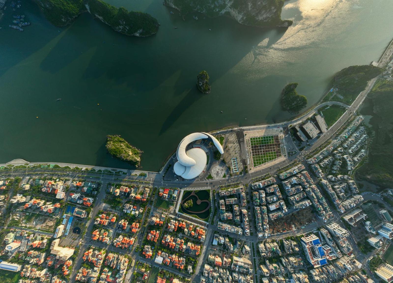 Aerial view of a curved white landmark building beside a lake within a city grid