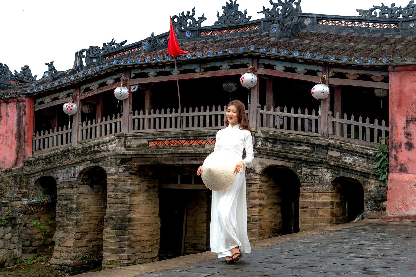 A woman in traditional Vietnamese attire stands by the Hoi An Japanese Bridge