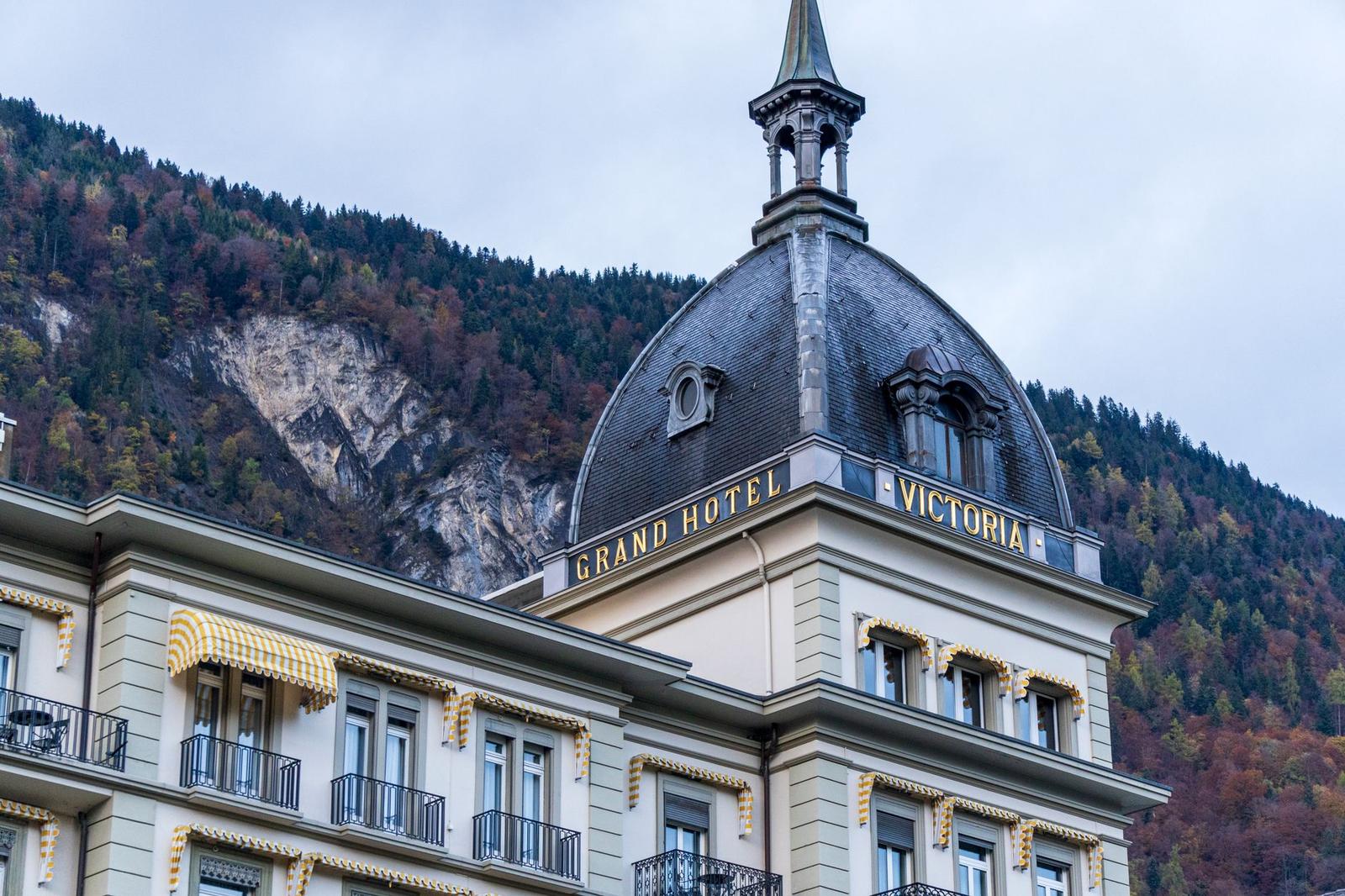 Cream hotel building with a domed tower and spire against a cloudy hillside