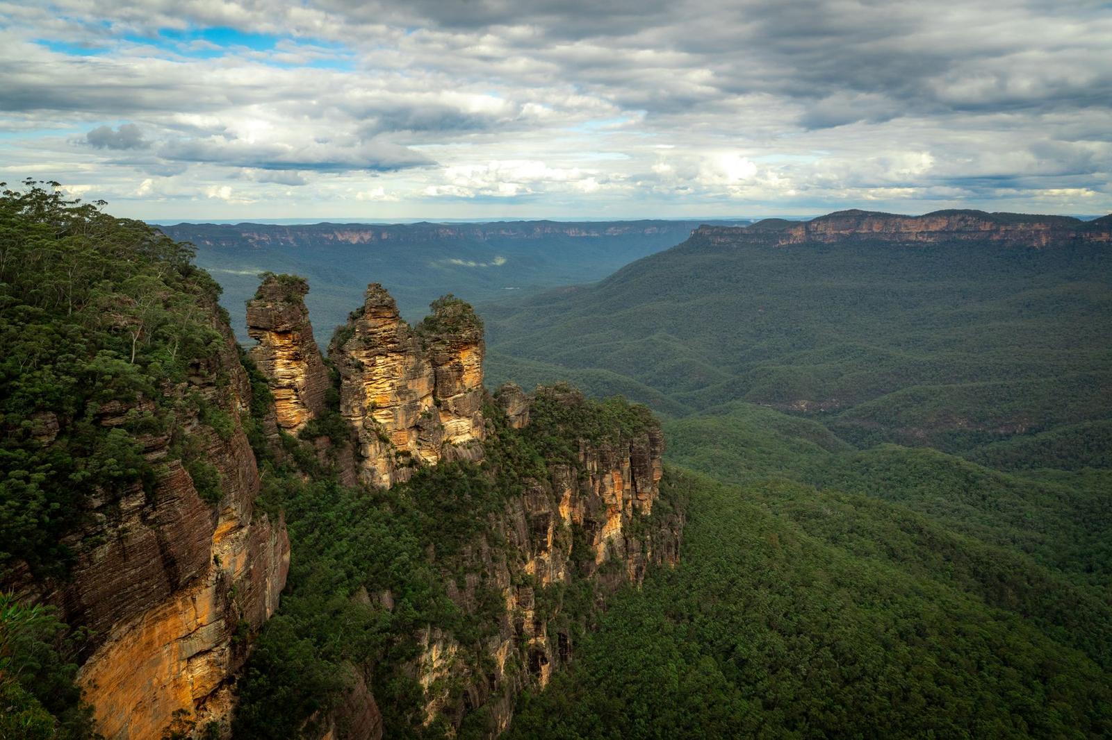 Three sandstone rock pinnacles rise from a forested cliff edge