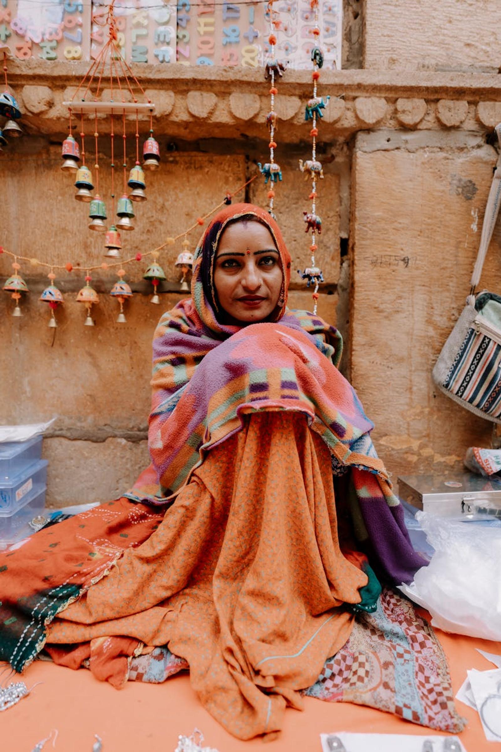 A woman in colorful traditional attire sits amidst handmade crafts in Jaisalmer, India