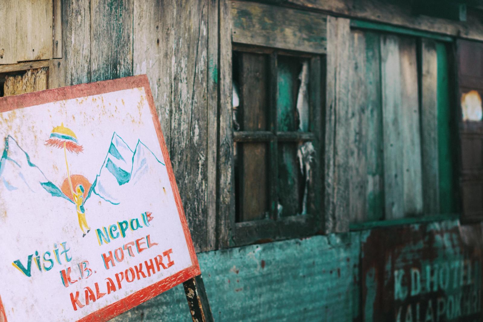 Rustic wooden sign outside LB Hotel in Kalipokhri, India promotes visiting Nepal