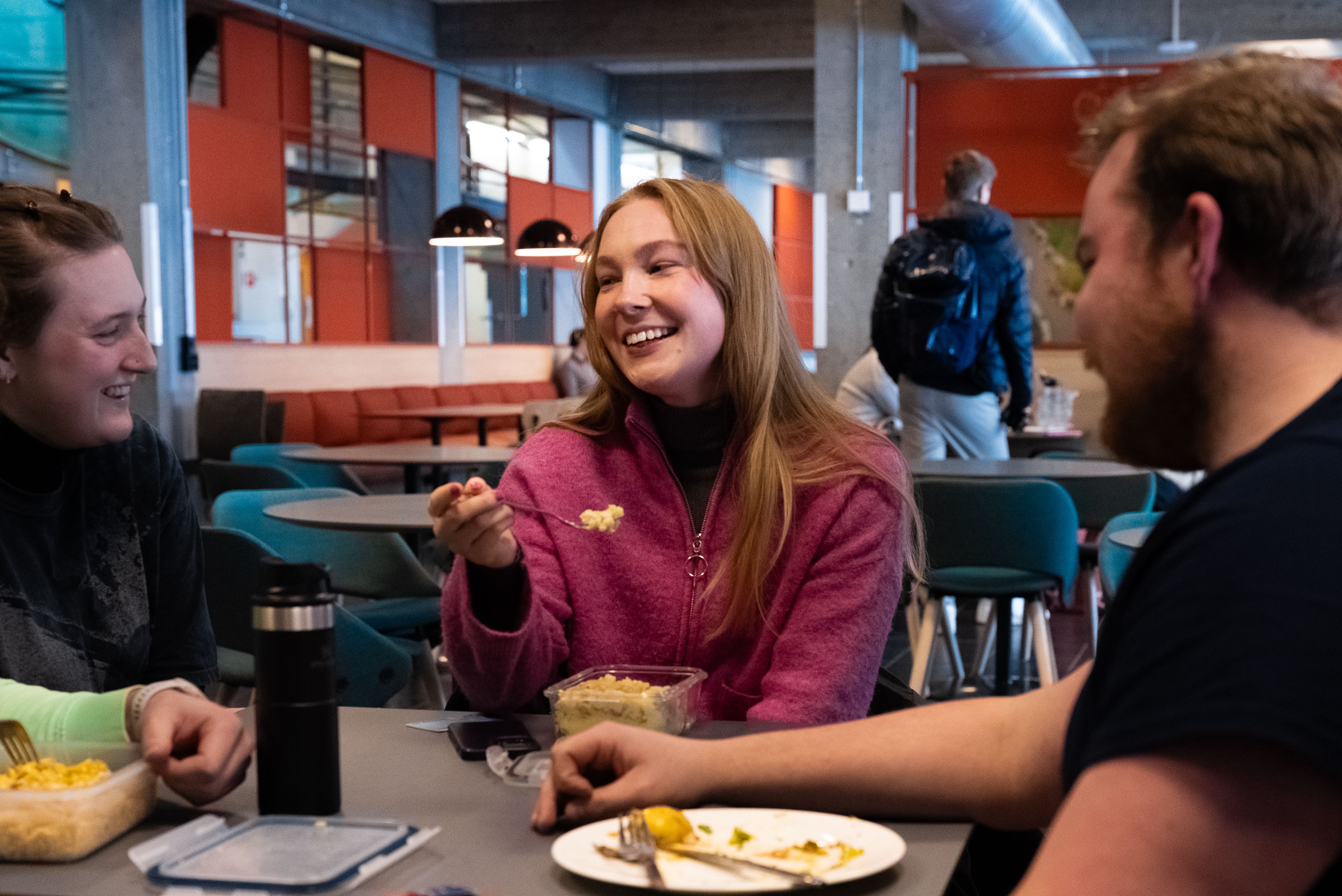 To studenter sitter sammen i kantine og spiser og snakker.