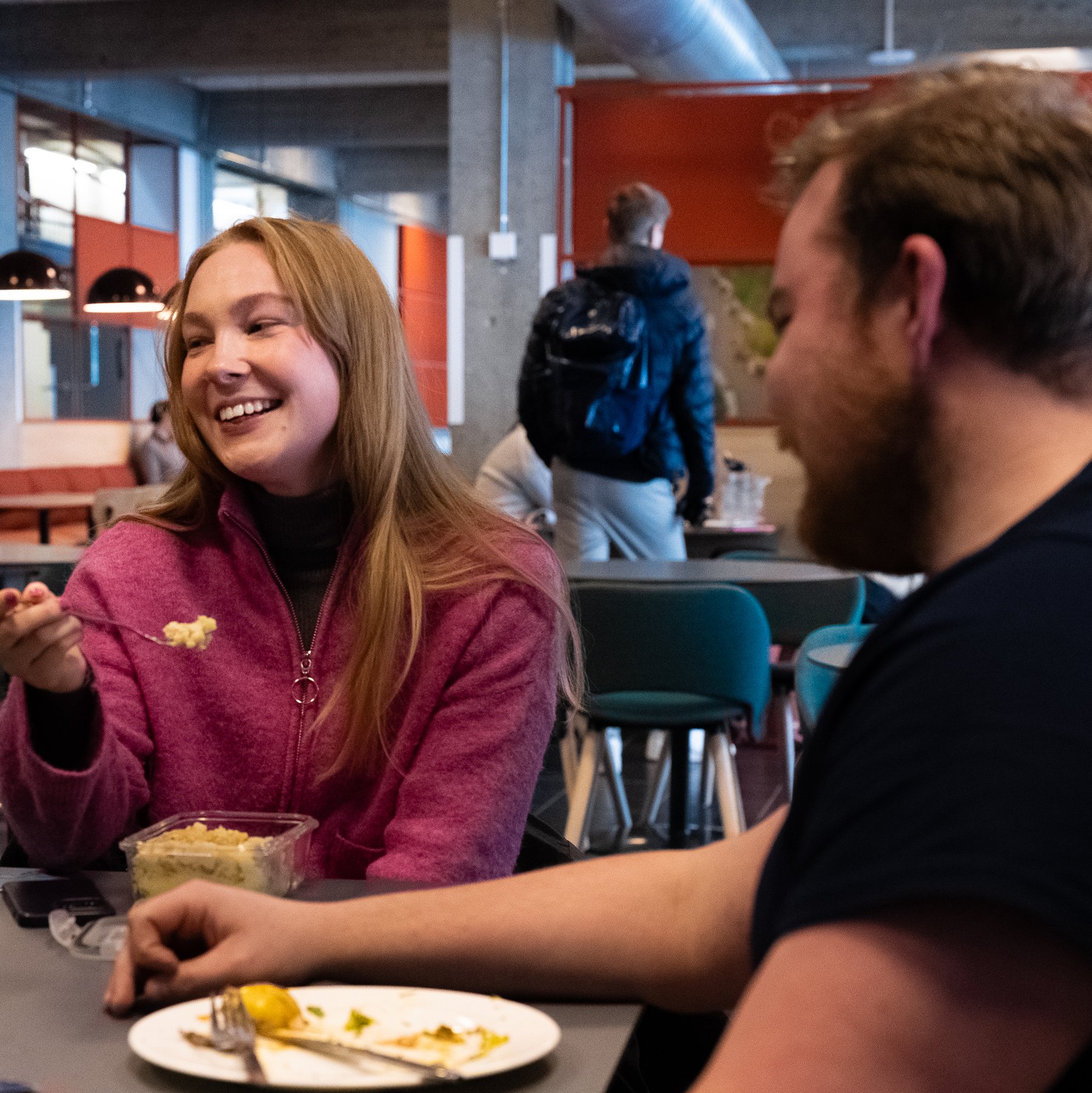 To studenter sitter sammen i kantine og spiser og snakker.