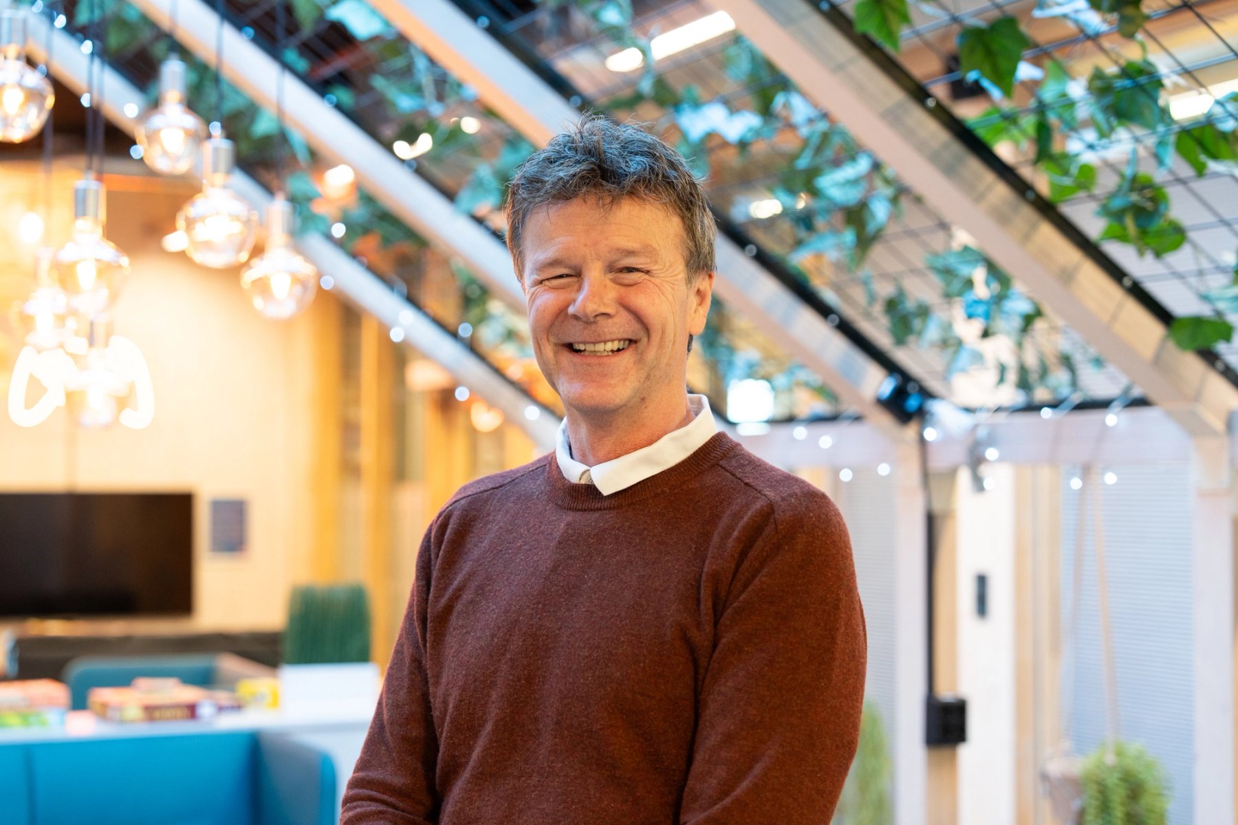 Frank Arntsen, eiendomsdirektør NTNU, står innendørs i et moderne fellesområde og smiler mot kamera.