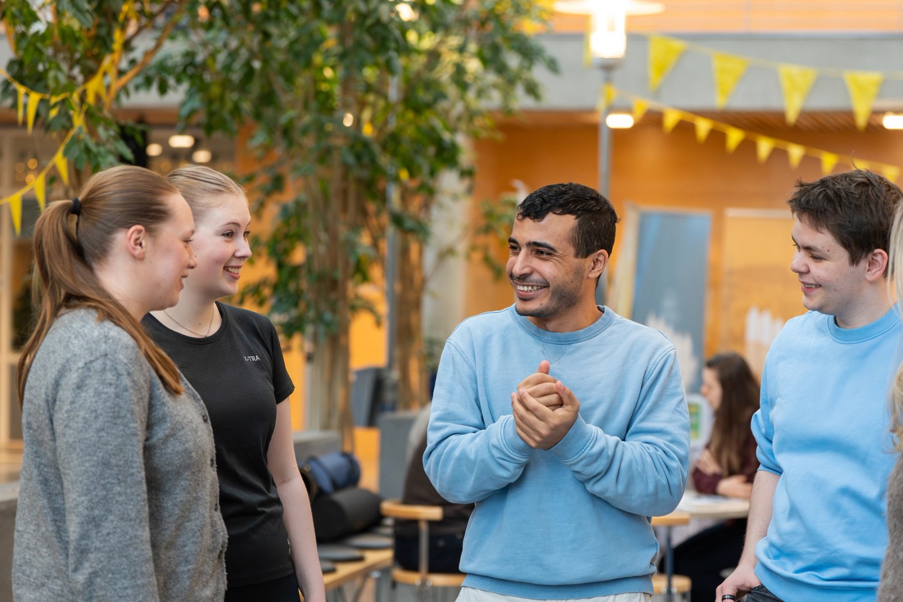 Fire studenter i samtale innendørs på campus, omgitt av grøntområde og sitteplasser.