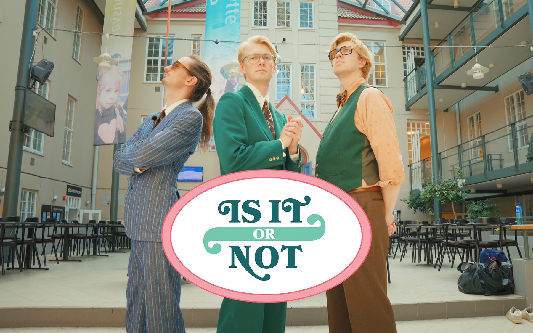 Tre personer i fargerike dresser står i en poserende trekantformasjon i et atrium. Midt i bildet vises logoen til gameshowet «Is It or Not».