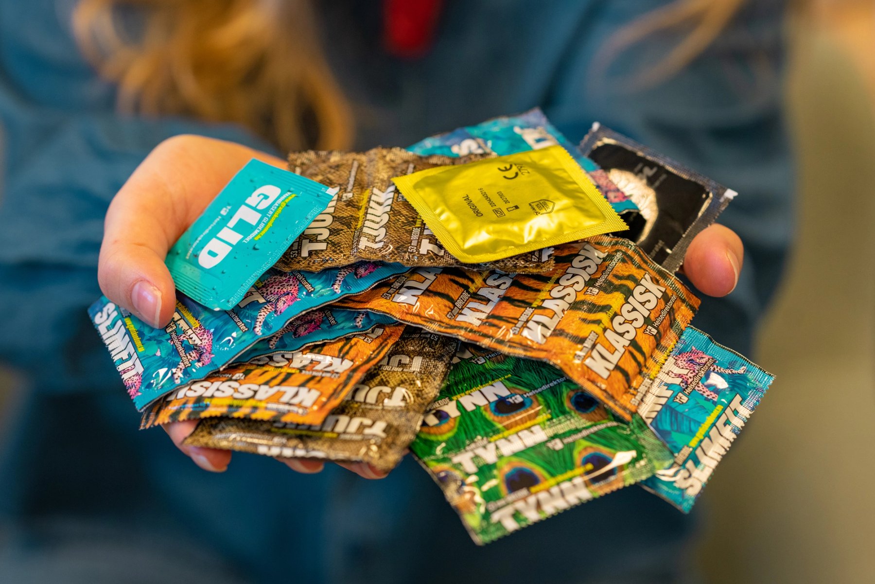 Bilde av hender som holder ulike typer kondomer i fargerike pakninger. 