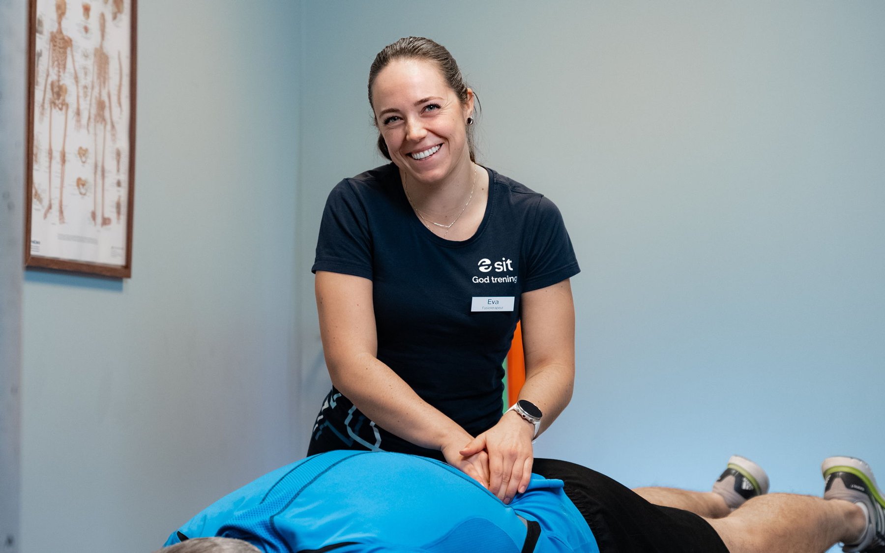 Photo of a smiling physiotherapist treating a patient lying face down in a treatment room.