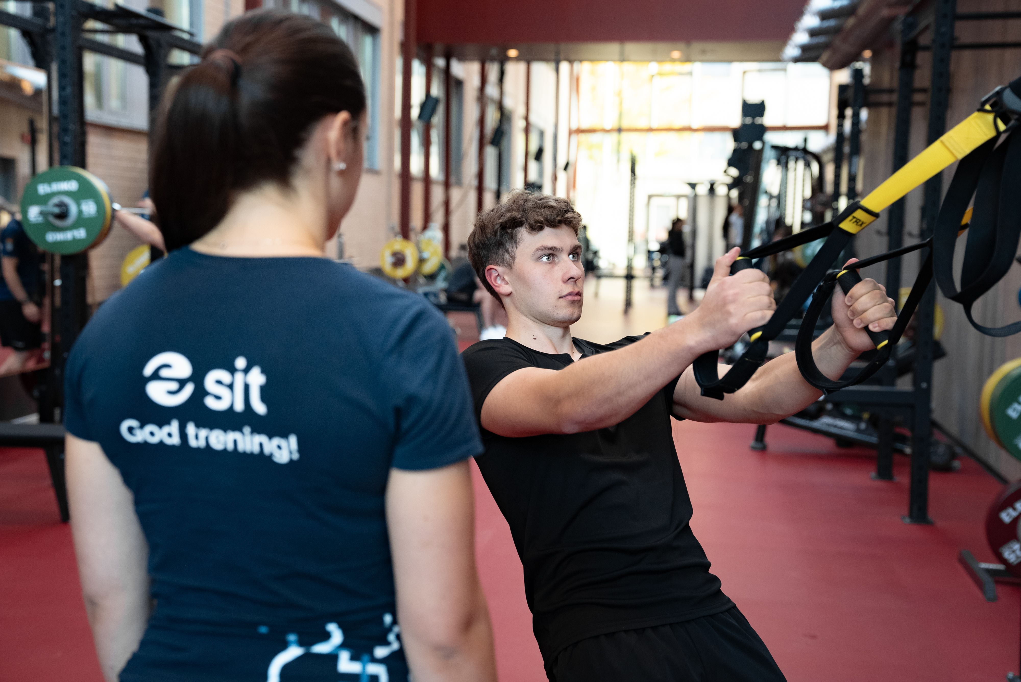 Personal trainer guiding a student in TRX pull exercise.