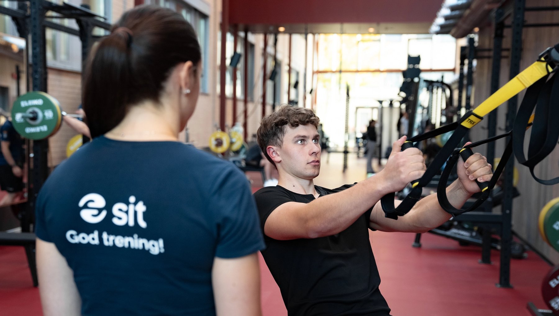 Personal trainer guiding a student in TRX pull exercise.