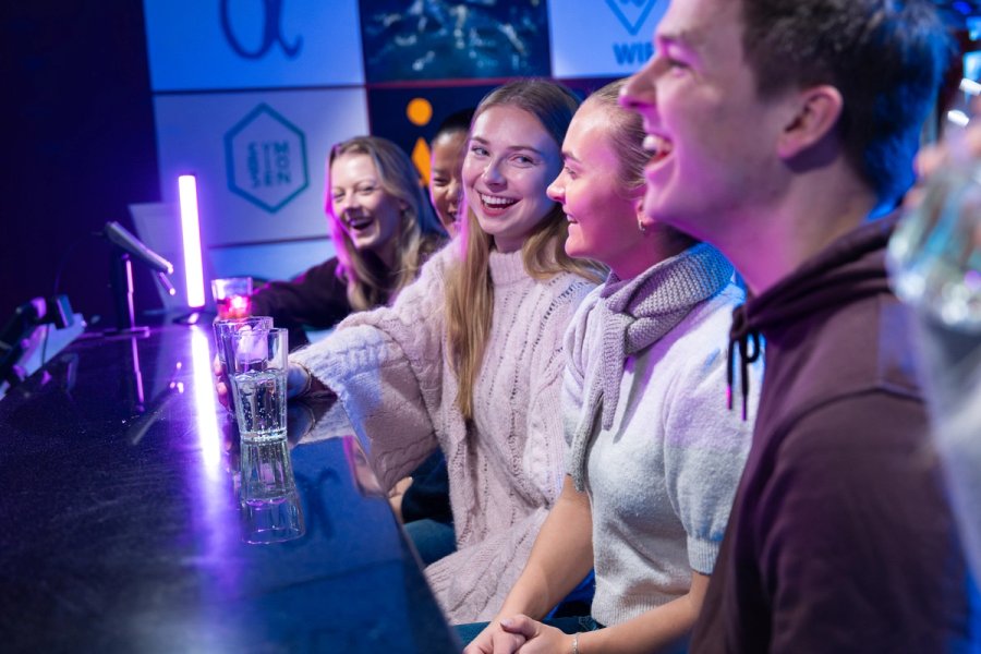 Flere studenter sitter i en bar og koser seg og smiler og ler og prater sammen med noen glass med drikke på disken