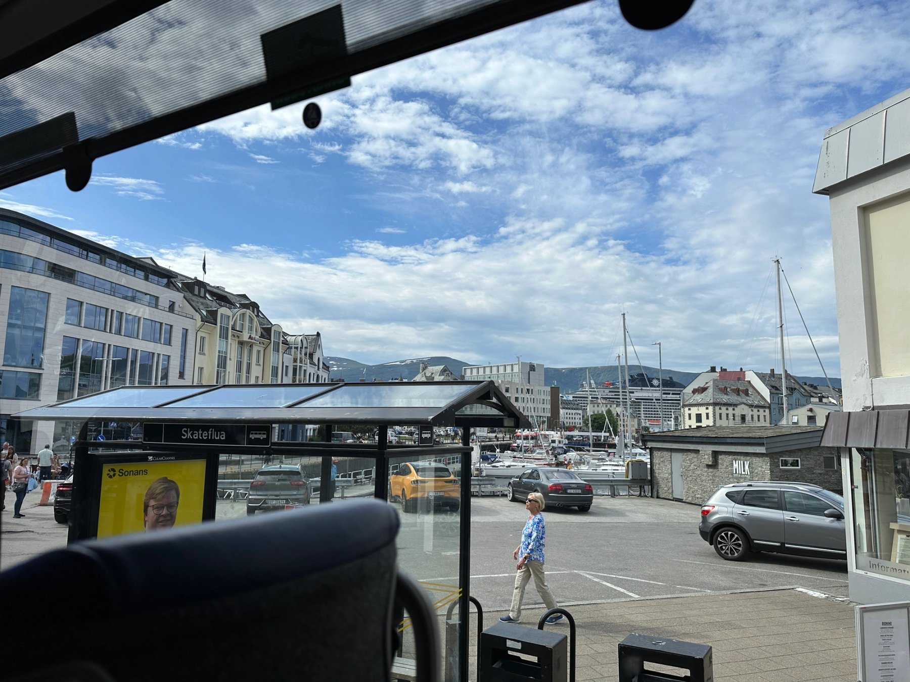 Et bilde tatt ut av et bussvindu det viser en brygge og en person som går i byen