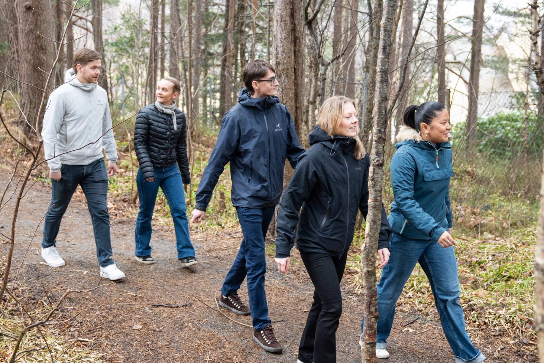 En gruppe studenter går sammen på en skogssti i rolig tempo, omgitt av trær og natur.