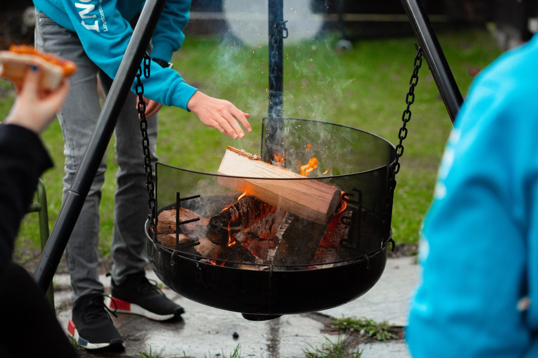 En student legger en vedkubbe oppi et tent bål i en bålpanne