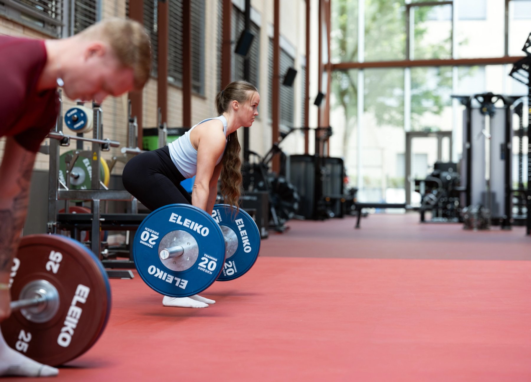 To personer som tar markløft på et rødt treningsgulv. 