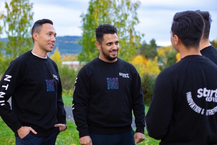 Fire studenter står utendørs og snakker sammen under et arrangement.