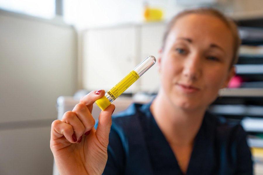 Bilde av helsesykepleier som holder opp et prøverør til testing ved Sits helsestasjon for seksuell helse.