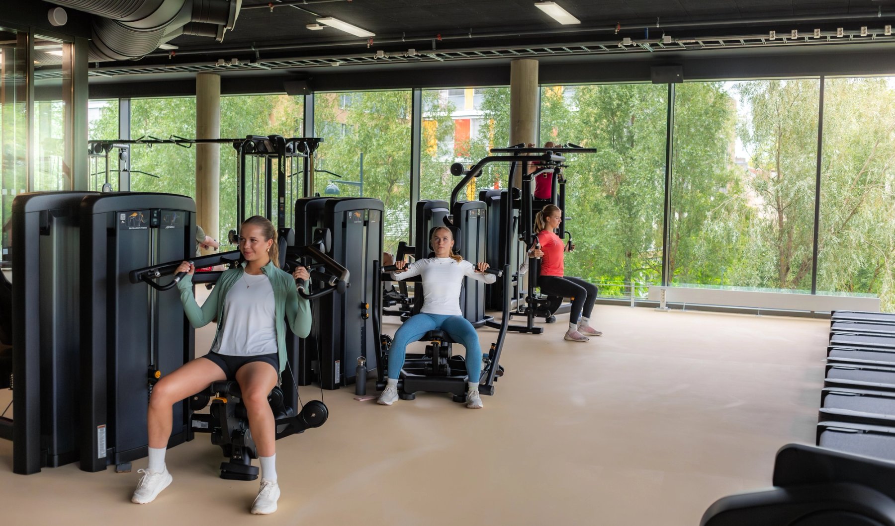 Tre jenter som trener styrke for overkropp i magasinapparater.